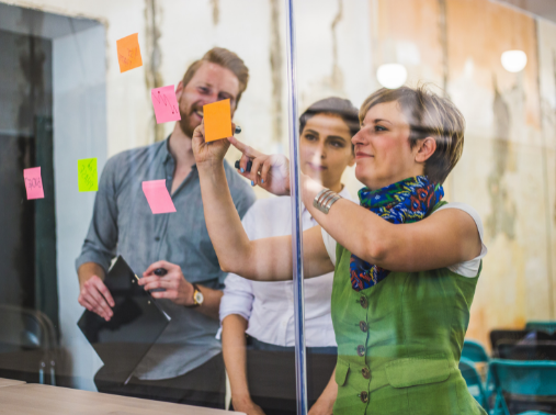 3 People reading and placing post it notes on a glass wall