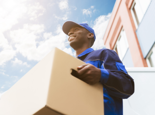 Taken from below a man dressed in delivery uniform carrying a cardboard box and smiling