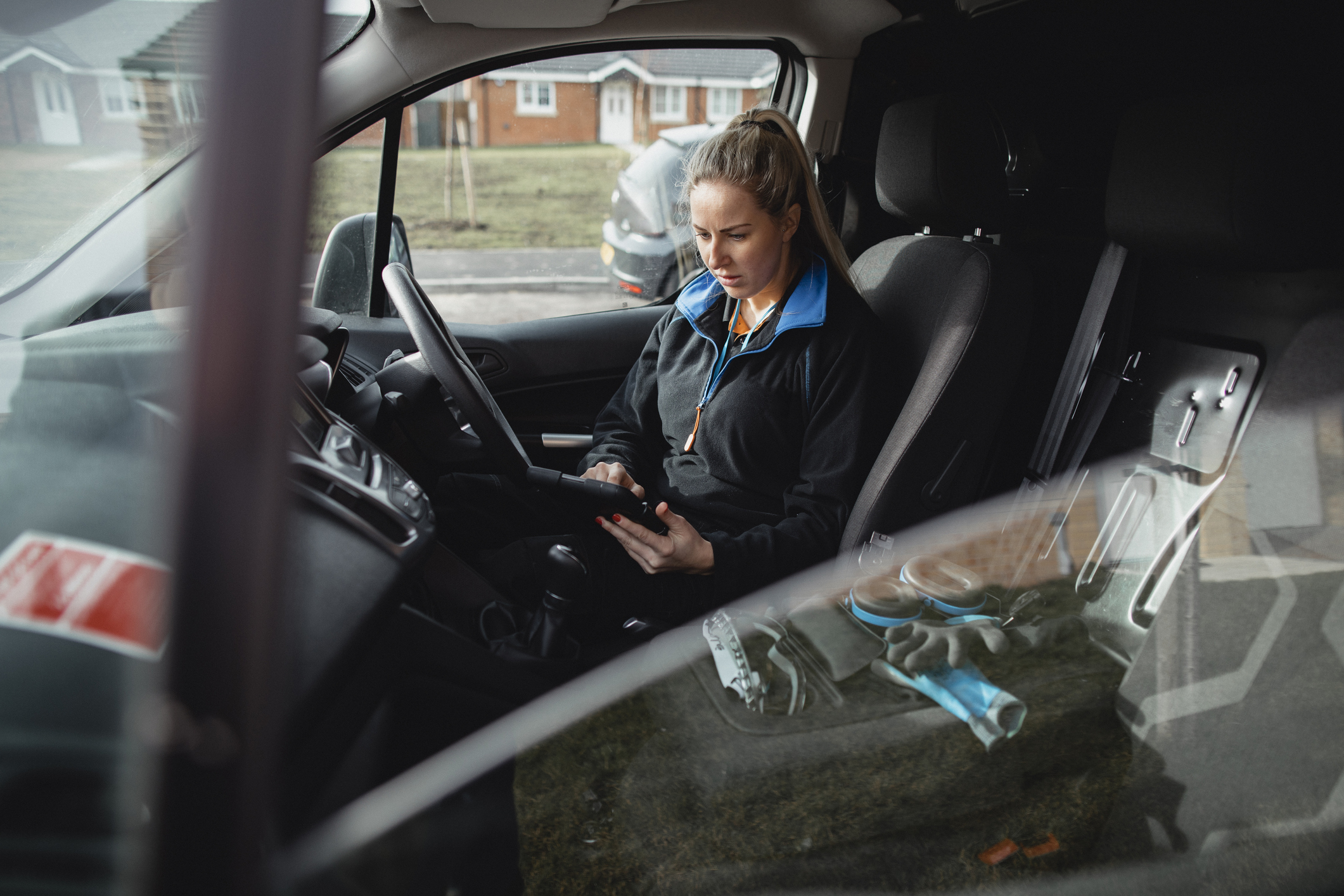 Female blue-collar worker sitting in her work van, using a digital tablet while working.